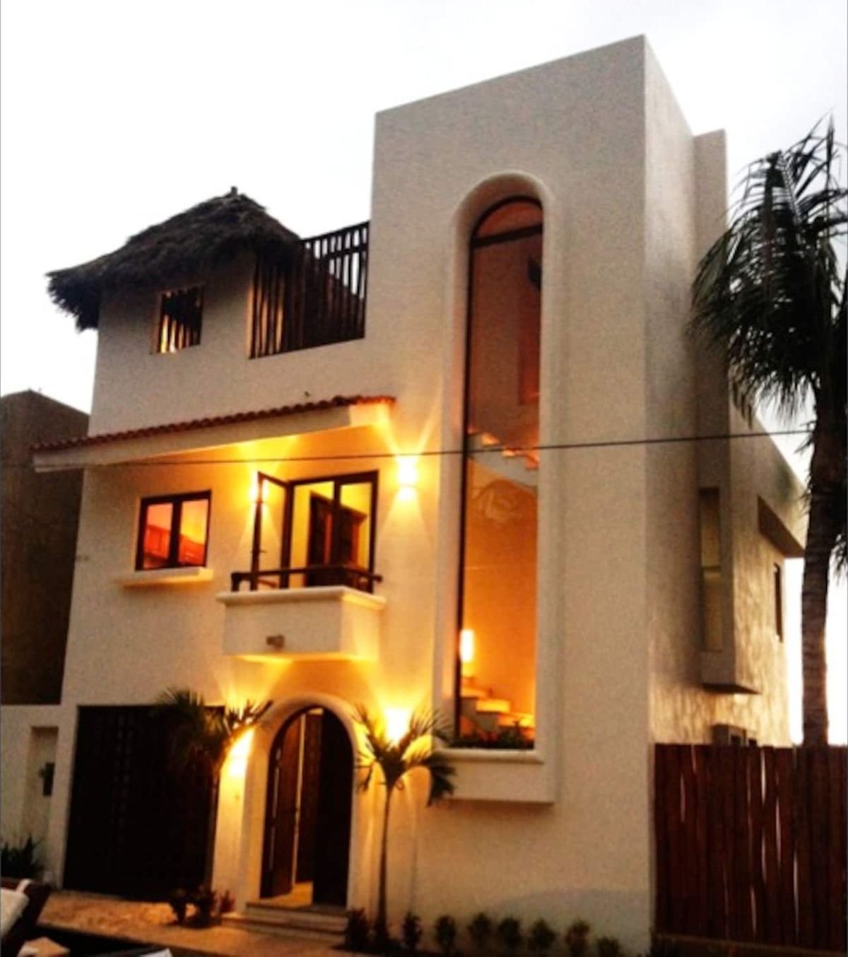 The front of Casa Luna Llena lit at dusk, with its tall arched window and palapa roof