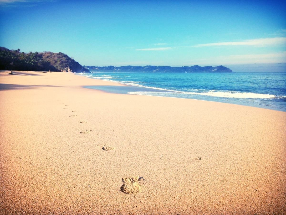 A wide, empty Sayulita beach with footprints in the sand